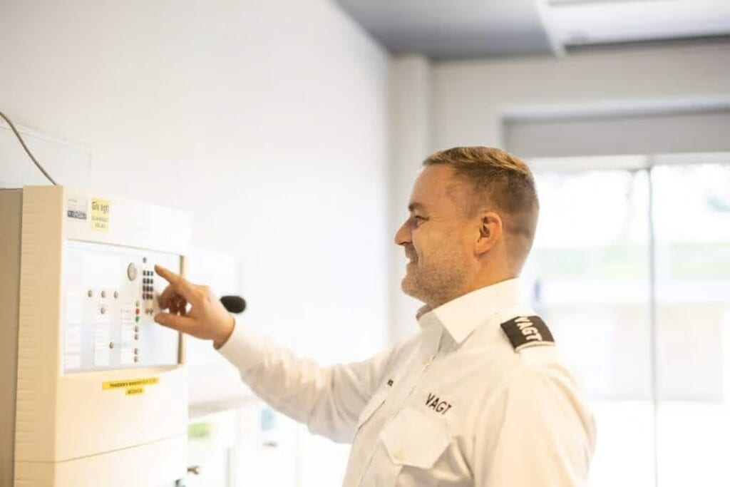 Mand i uniform betjener sikkerhedssystem i kontrolrum.
