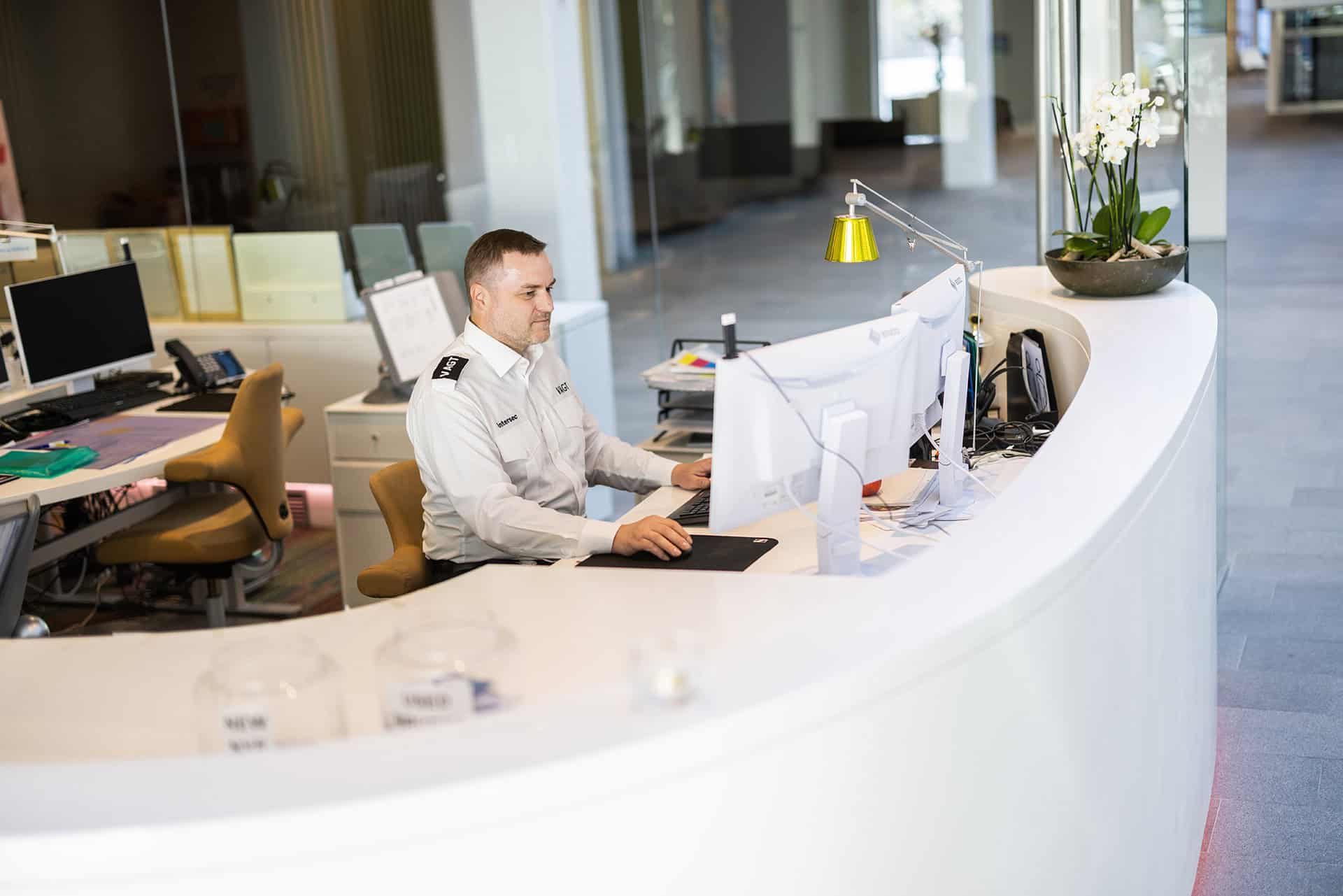 Mand arbejder ved receptionen i et moderne kontor med computerskærme.